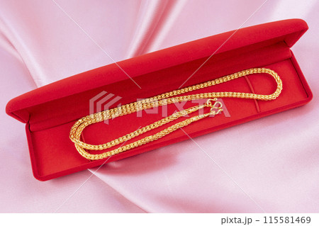 Gold Necklace in red velvet box container on pink fabric background. Gold Necklace in red velvet box container on pink fabric background. 115581469
