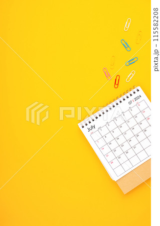 July 2024 desk calendar and paper clips on yellow color background. 115582208