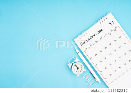 November 2024, Monthly desk calendar for 2024 year and alarm clock with paper clips on blue color. 115582212