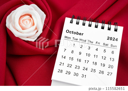 October 2024 desk calendar and pink rose on red textile. October 2024 desk calendar and pink rose on red textile. 115582651