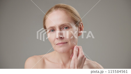 Anti age, Beauty, health and dry skin care concept - beautiful middle-aged mature Caucasian woman in her 50s touching her face skin and looking at the camera with a slight smile 115584561