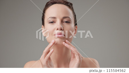 Beauty, health, cosmetics, anti-aging therapy and skin care concept - young beautiful brunette Caucasian woman touching face and looking at camera Beauty, health, cosmetics, anti-aging therapy and skin care concept - young beautiful brunette Caucasian woman touching face and looking at camera 115584562