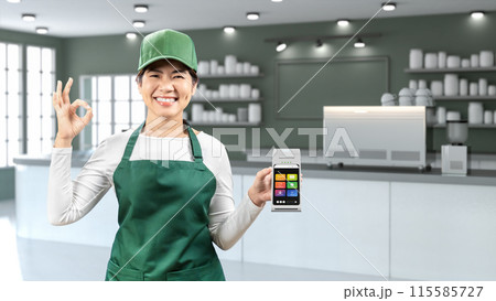 Asian seller wear green apron and green cap smiling with hand holding card reader Asian seller wear green apron and green cap smiling with hand holding card reader 115585727