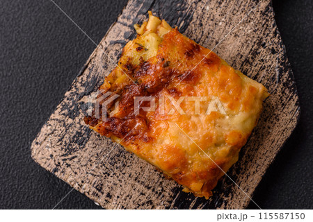 Delicious baked lasagna pasta with meat, sauce, salt, spices and herbs on a dark concrete background 115587150