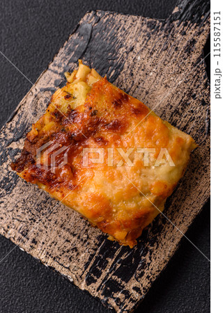 Delicious baked lasagna pasta with meat, sauce, salt, spices and herbs on a dark concrete background 115587151