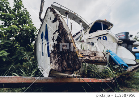 Old and rusty motor boats on a landfill surrounded by tropical forest 115587950
