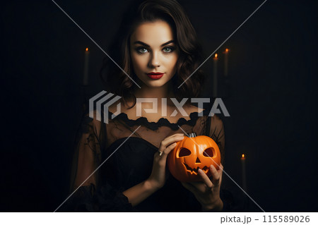In a dark room, a mysterious woman in black holds a Halloween pumpkin under candlelight 115589026