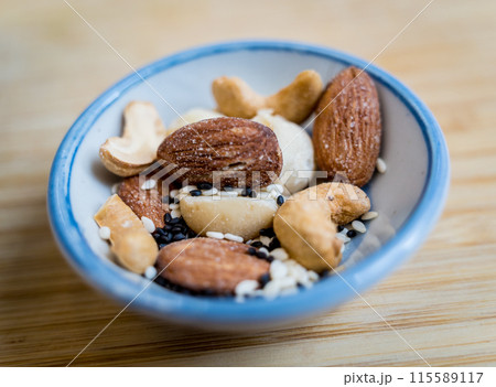 A bowl filled with assorted nuts and seeds is placed on a rustic wooden table A bowl filled with assorted nuts and seeds is placed on a rustic wooden table 115589117