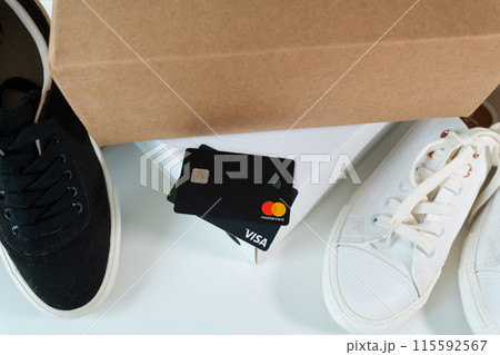 A credit card lies between a black sneaker and a white sneaker, next to an open cardboard box. A credit card lies between a black sneaker and a white sneaker, next to an open cardboard box. 115592567