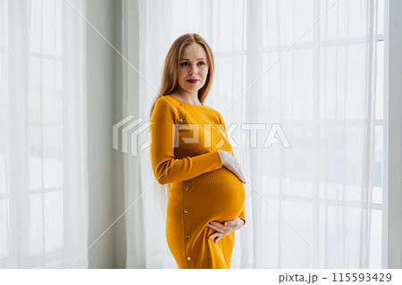 Pregnancy motherhood people expectation future. Pregnant woman with big belly standing near window at home. Girl hugging her tummy enjoying pregnancy. Maternity tenderness parenthood new life concept Pregnancy motherhood people expectation future. Pregnant woman with big belly standing near window at home. Girl hugging her tummy enjoying pregnancy. Maternity tenderness parenthood new life concept 115593429