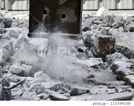A hydraulic hammer breaking concrete at a construction site 115594100