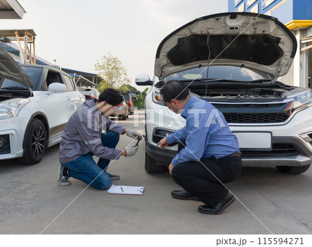 Two individual inspect damage on a vehicle. Car owner pointing at a dent on the bumper of the car. An insurance staff taking picture with smartphone, conducting an assessment related to the damage. Two individual inspect damage on a vehicle. Car owner pointing at a dent on the bumper of the car. An insurance staff taking picture with smartphone, conducting an assessment related to the damage. 115594271