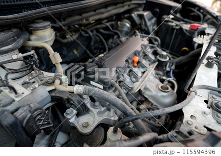 Closeup view of a car engine with various component and wire visible under the hood. 115594396