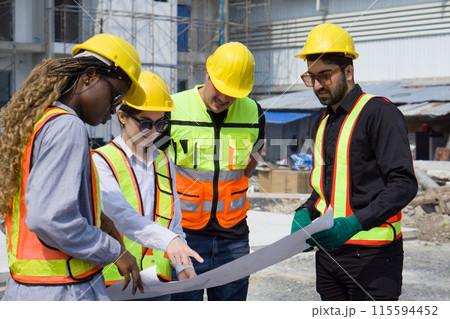 Group of construction workers gathered at a construction site reviewing some plan. Unfinished building, piles of construction material, and a partially constructed structure are in the background Group of construction workers gathered at a construction site reviewing some plan. Unfinished building, piles of construction material, and a partially constructed structure are in the background 115594452