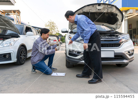 Two individual inspect damage on a vehicle. Car owner pointing at a dent on the bumper of the car. An insurance staff taking picture with smartphone, conducting an assessment related to the damage. Two individual inspect damage on a vehicle. Car owner pointing at a dent on the bumper of the car. An insurance staff taking picture with smartphone, conducting an assessment related to the damage. 115594455
