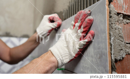 Instaling ceramic tiles. Male hands glue ceramic tiles on the wall in the bathroom. 115595881