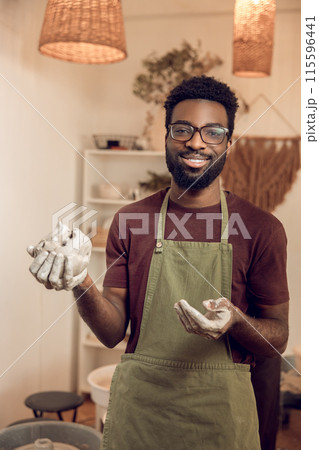 African american smiling sculptor with wet clay in hands looking contented African american smiling sculptor with wet clay in hands looking contented 115596441