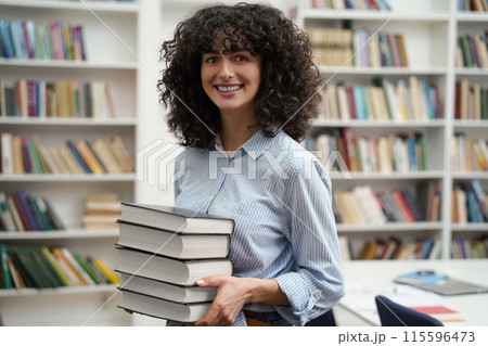 Pretty woman carrying a pile of books and smiling nicely 115596473
