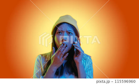 Shocking call. Bad news. Blue color neon light astonished woman use phone talk surprised overwhelmed expression isolated on orange gradient empty space background. 115596960