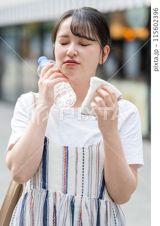 若くて可愛い日本人女性が屋外でタオルで汗を拭きながら水分補給｜熱中症対策イメージ｜水分補給イメージ 115602396