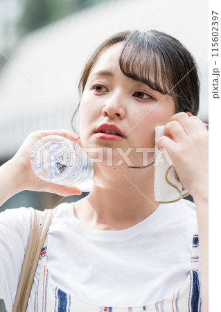 若くて可愛い日本人女性が屋外でタオルで汗を拭きながら水分補給｜熱中症対策イメージ｜水分補給イメージ 115602397
