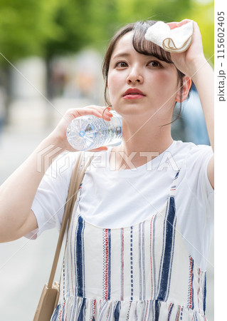 若くて可愛い日本人女性が屋外でタオルで汗を拭きながら水分補給｜熱中症対策イメージ｜水分補給イメージ 115602405