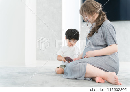 スマホを見る男の子と子守をする妊娠中のママ・母親 スマホを見る男の子と子守をする妊娠中のママ・母親 115602805