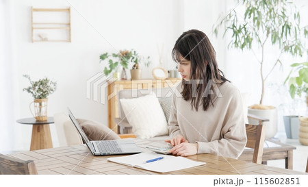電卓で計算してメモをする女性 115602851