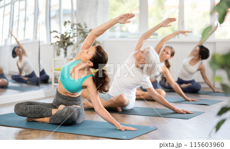 Woman performing side stretch in easy pose during group yoga practice 115603960