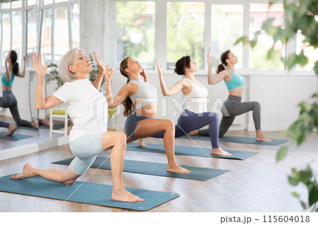 Woman standing yoga pose and making full body stretching workout with group in room Woman standing yoga pose and making full body stretching workout with group in room 115604018