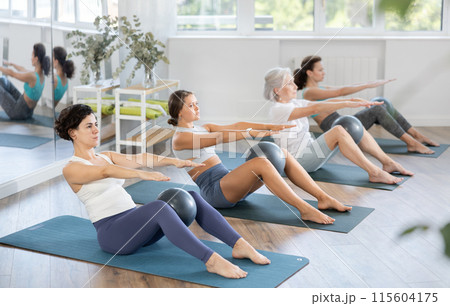 Latina doing sit-ups with ball during group Pilates session 115604175