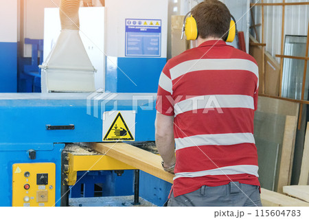 A man is seen operating a large, blue carpentry machine with caution and focus in a professional A man is seen operating a large, blue carpentry machine with caution and focus in a professional 115604783