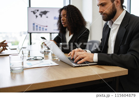 Business meeting with colleagues working on laptops in office 115604879