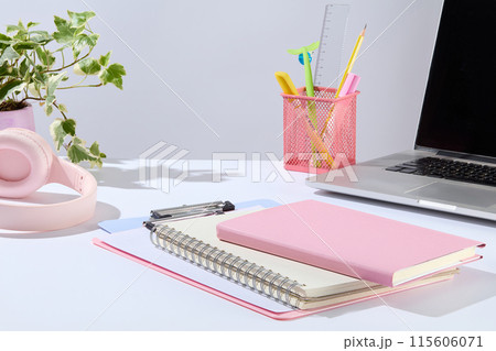 Office concept photo from front view, over white background. In the middle of white tabletop contains some notebook and clipboard, next to a laptop, pen pot, and a pink headphone. Space for designing Office concept photo from front view, over white background. In the middle of white tabletop contains some notebook and clipboard, next to a laptop, pen pot, and a pink headphone. Space for designing 115606071