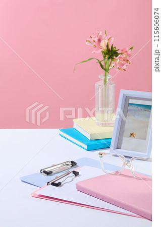 Pink background photo was shot from above view, white desk containing some essential stationery for working, decorated with a glass flower vase and blue frame picture. Space for product presentation Pink background photo was shot from above view, white desk containing some essential stationery for working, decorated with a glass flower vase and blue frame picture. Space for product presentation 115606074
