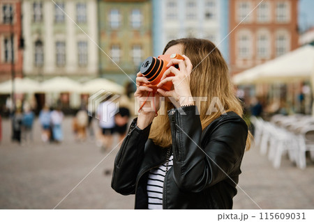 Woman taking picture using orange instant camera. Tourist captures memories during travel with vintage camera. Female walking around city street Woman taking picture using orange instant camera. Tourist captures memories during travel with vintage camera. Female walking around city street 115609031