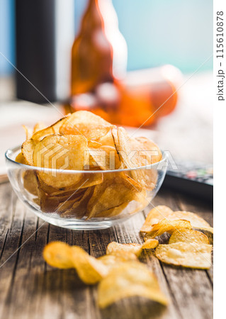 Bowl of Potato Chips on Wooden Table With Remote and Beer Bottles 115610878