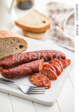 Sliced smoked salami sausage on wooden cutting board on white table. Sliced smoked salami sausage on wooden cutting board on white table. 115610895