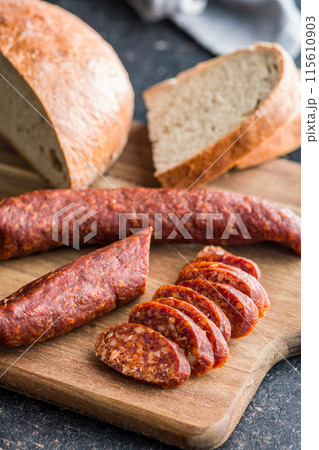 Sliced smoked salami sausage on wooden cutting board on black table. 115610903
