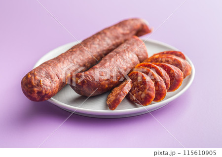 Sliced smoked salami sausage on plate on violet background. 115610905
