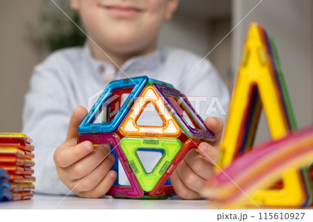 Child playing with magnetic constructor, hands close-up. 115610927