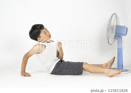 部屋で小学生の男の子がランニングシャツを着て、扇風機の前で暑くてぐったりしている様子 115611826