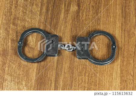 Police handcuffs lie on a wooden table 115613632