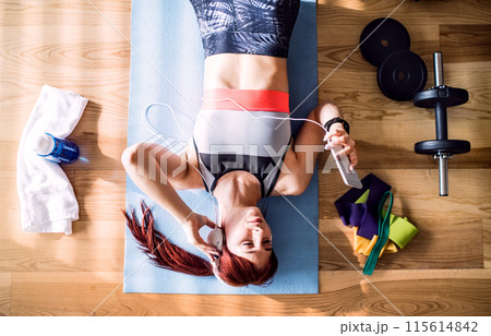 Beautiful redhead woman's home workout routine with dumbbell. Home fitness workout in living room, sporty woman wearing sportswear. Beautiful redhead woman's home workout routine with dumbbell. Home fitness workout in living room, sporty woman wearing sportswear. 115614842