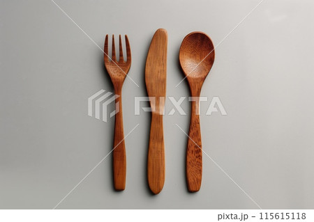 Minimalist arrangement of wooden fork, knife, and spoon isolated on a gray backdrop 115615118
