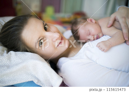 New mom lying on bed by newborn baby girl. Unconditional paternal love, idyllic family moment. New mom lying on bed by newborn baby girl. Unconditional paternal love, idyllic family moment. 115615473