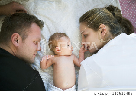 New parents lying on bed by newborn baby girl. Unconditional paternal love, idyllic family moment. New parents lying on bed by newborn baby girl. Unconditional paternal love, idyllic family moment. 115615495