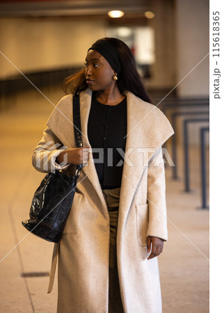 Elegant woman in a stylish coat confidently strolling indoors, exuding glamour and sophistication Elegant woman in a stylish coat confidently strolling indoors, exuding glamour and sophistication 115618365