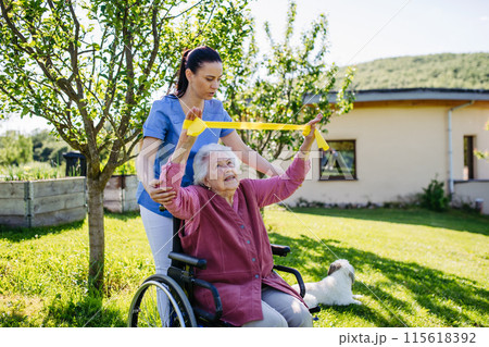 Female caregiver doing motorized exercises with senior woman in wheelchair. Nurse and elderly woman working out with resistance band. Female caregiver doing motorized exercises with senior woman in wheelchair. Nurse and elderly woman working out with resistance band. 115618392