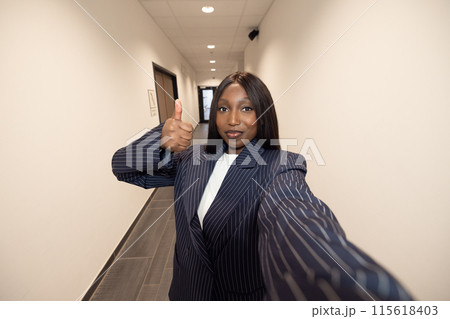 A professional woman showing approval with a thumbsup gesture in a modern office hallway 115618403